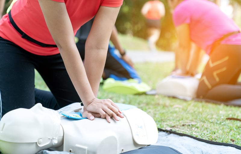 Asian Female Or Runner Woman Training Cpr Demonstrating Class In Park By Put Hands And Interlock Finger Over Cpr Doll Give Chest Compression. First Aid Training For Heart Attack People Or Lifesaver.