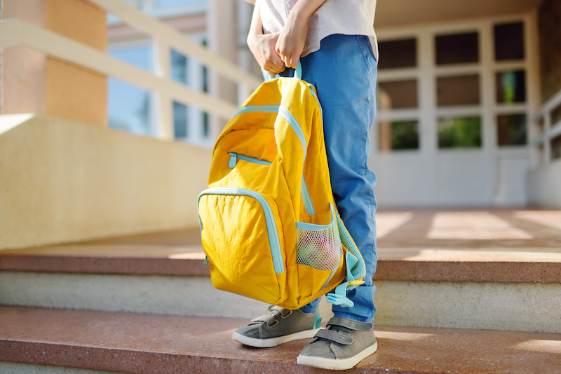 Little Student With A Backpack On The Steps Of The Stairs Of School Building. Close Up Of Child Legs, Hands And Schoolbag Of Boy Standing On Staircase Of Schoolhouse.back To School Concept.