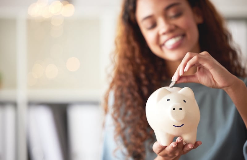One Happy Young Mixed Race Woman Holding A Piggybank And Depositing A Coin As Savings. Hispanic Woman Budgeting Her Finances And Investing Money Into Her Future. Saving Funds For Financial Freedom