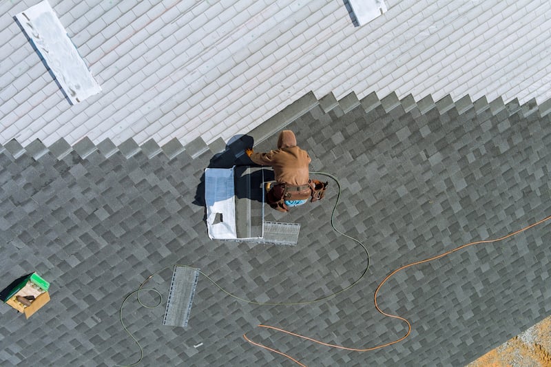 A Worker Uses An Air Hammer To Nail New Roof Shingles To Bitumen Using A Top View From Above