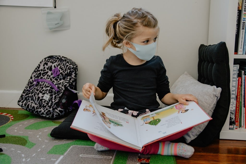 A young girl reading a book, wearing sock near a book shelf