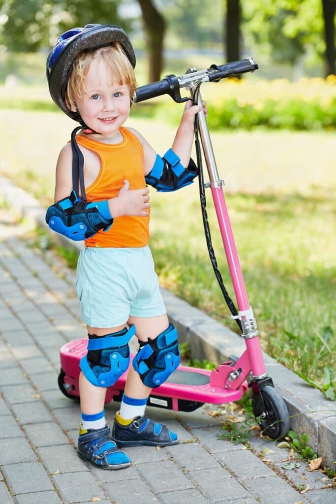 Little,boy,in,protective,equipment,with,electrical,scooter,in,park