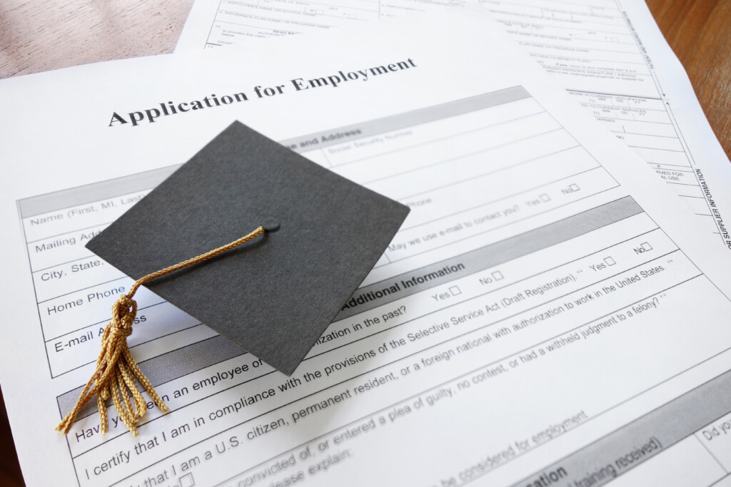 Managing recent graduates photo — mini graduation cap on a job application form