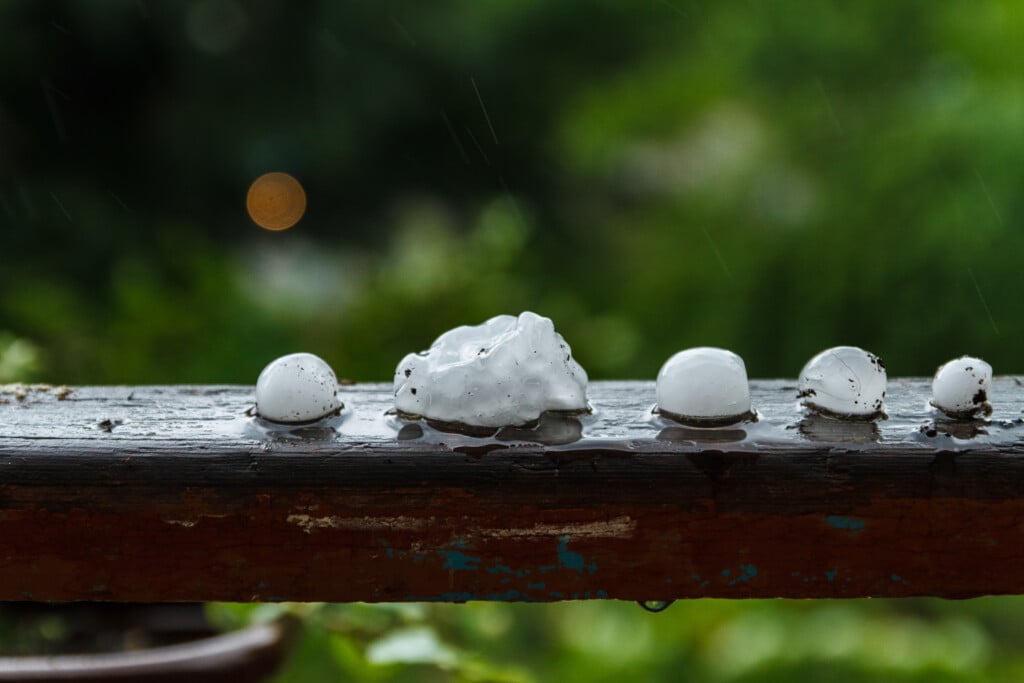 Hail Season: Pieces of ice on the wooden railing on a blurred background after hailstorm.