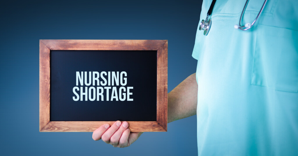 Nursing Shortage. Doctor Shows Sign/board With Wooden Frame. Bac