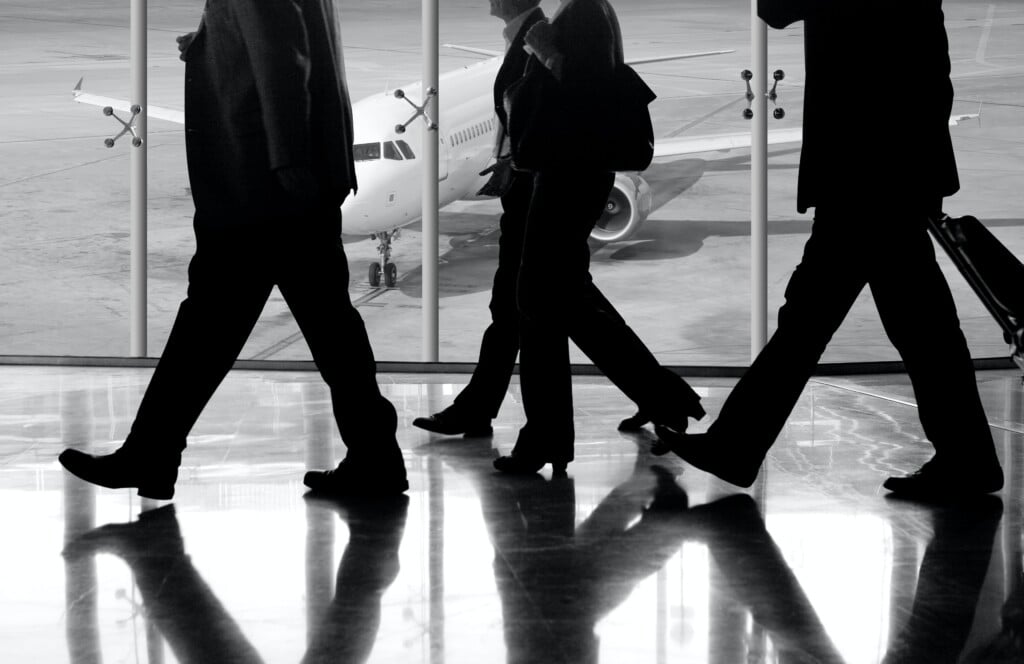 Business Travel and Mental Health represented by a black and white photo of 3 business men walking in an airport