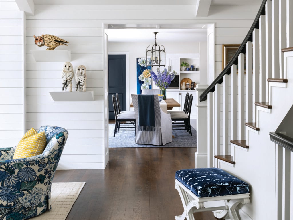 Entry Wooden owls by Maine artist Dan Falt take perch in the entryway, overlooking a CR Laine ottoman and chair upholstered in Schumacher fabric. The dining room features a Visual Comfort chandelier and a rug from Serena & Lily. | Photo: Kimberly Gavin
