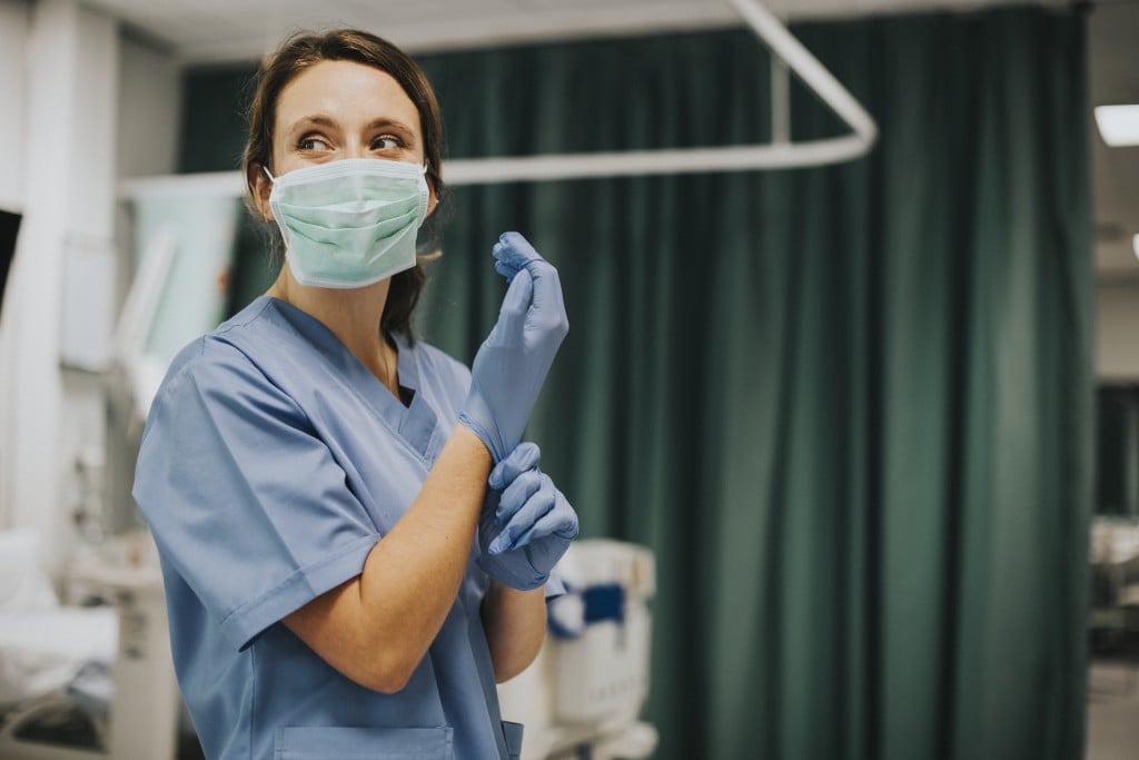 Nurse Putting On Gloves In Hospital Room