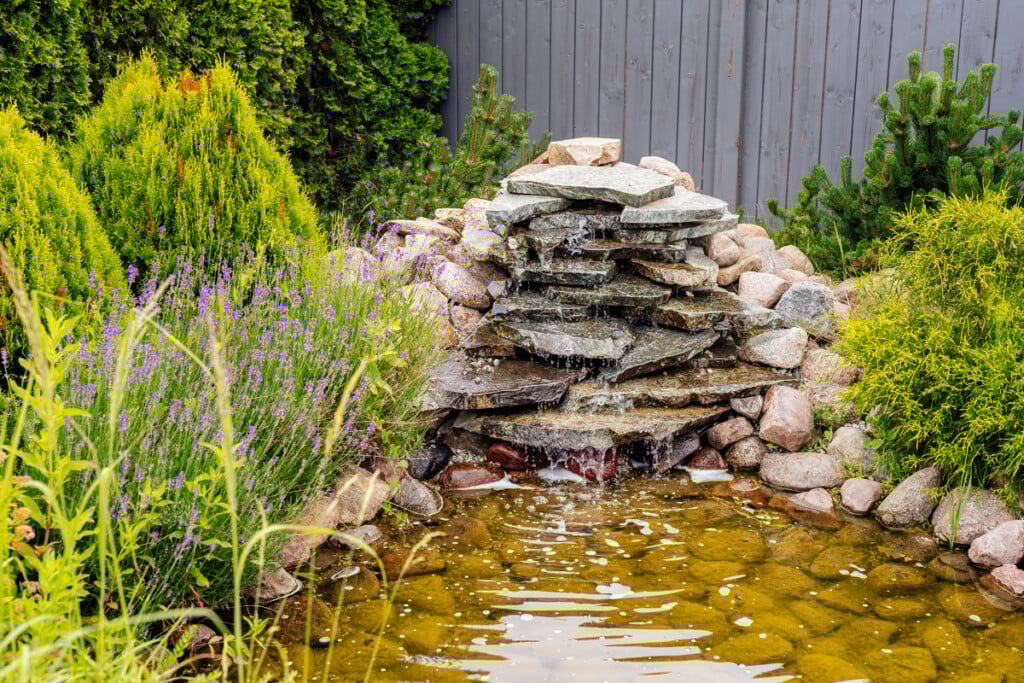 Stone Waterfall With A Pond And Flowers