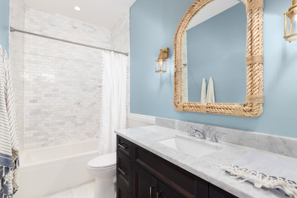 A Bathroom With Blue Walls, Gold Sconces, And Tiled Shower.