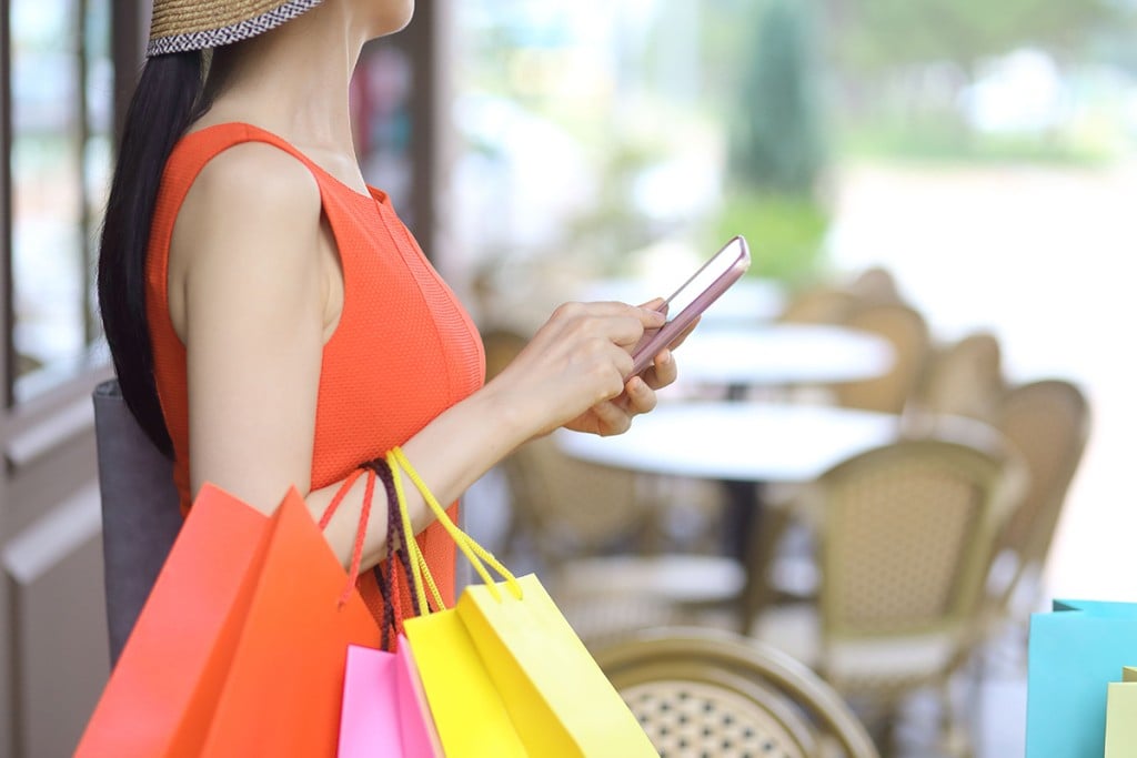 Woman Using Smartphone With Shopping Bags At Sidewalk Cafe