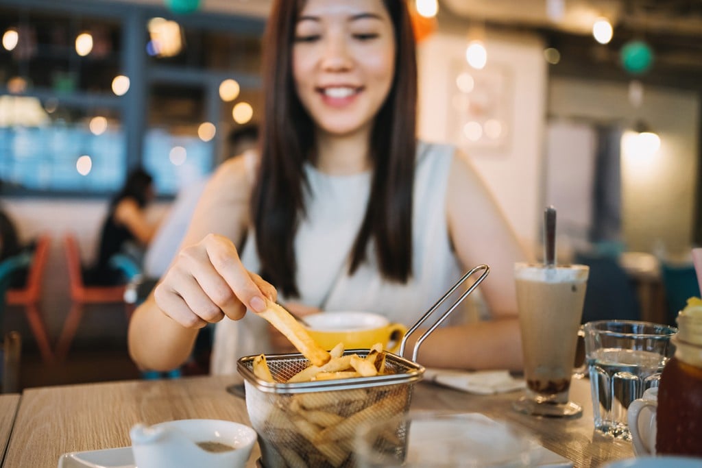 Cheerful Young Woman Sitting In Restaurant And Eating French Fries