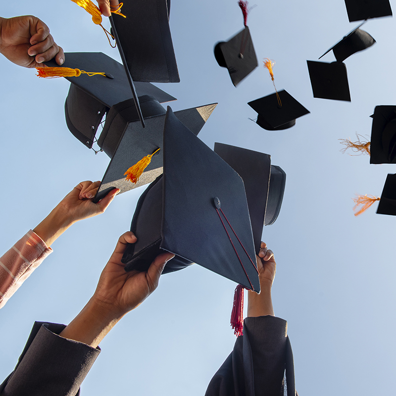 Cropped Hands Of People Throwing Mortarboards Against Clear Sky