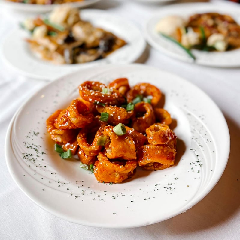 Calamari covered in sauce on a white plate sprinkled with herbs