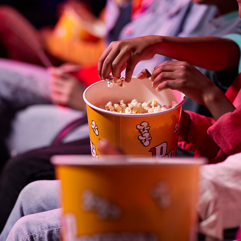 Midsection Of Friends Sharing Popcorn While Sitting In Theater
