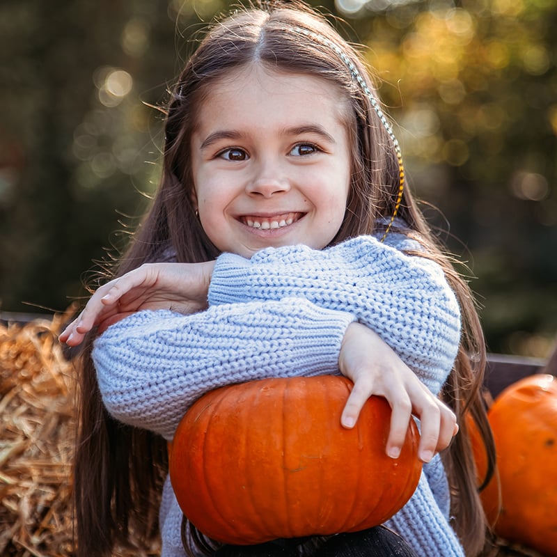 Autumn Harvest Of Pumpkins. Child And Orange Pumpkin At Farm Market Or Seasonal Festival. Cute Little Girl Playing Among Pumpkins. Thanksgiving Holiday Season And Halloween.