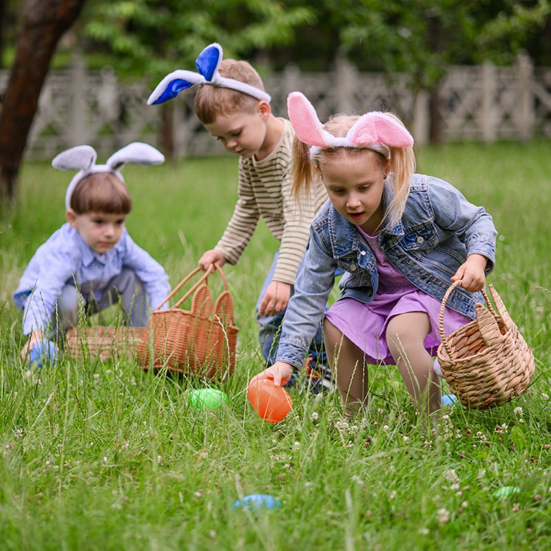 Children Wearing Bunny Ears Collecting Easter Eggs Outdoors In Spring