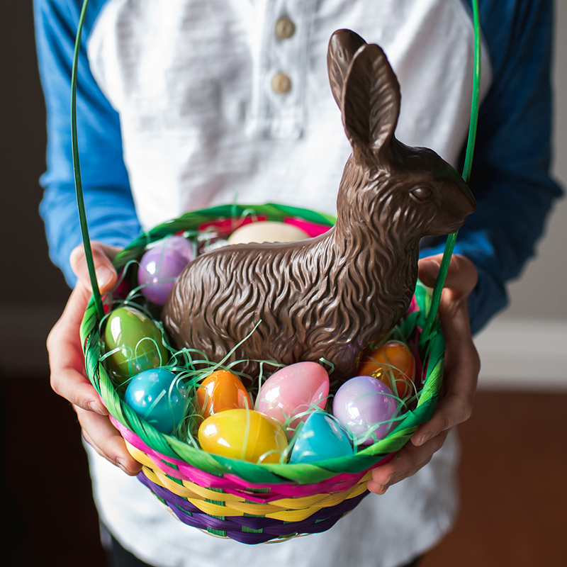 Close Up Of Child's Hands Holding An Easter Basket Full Of Treats.