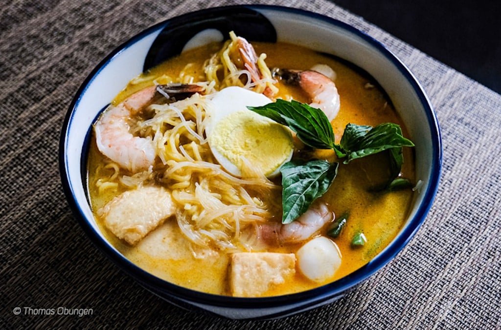 loaded bowl of laksa noodle soup with shrimp, herbs, egg and more