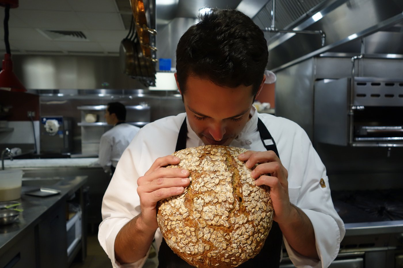 Berkley Spivey in the kitchen at Vintage Cave, smelling a fresh-baked loaf of bread out of the oven.
