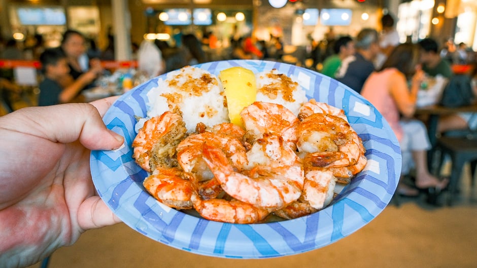 a plate of garlic butter shrimp in the foreground of a packed food hall