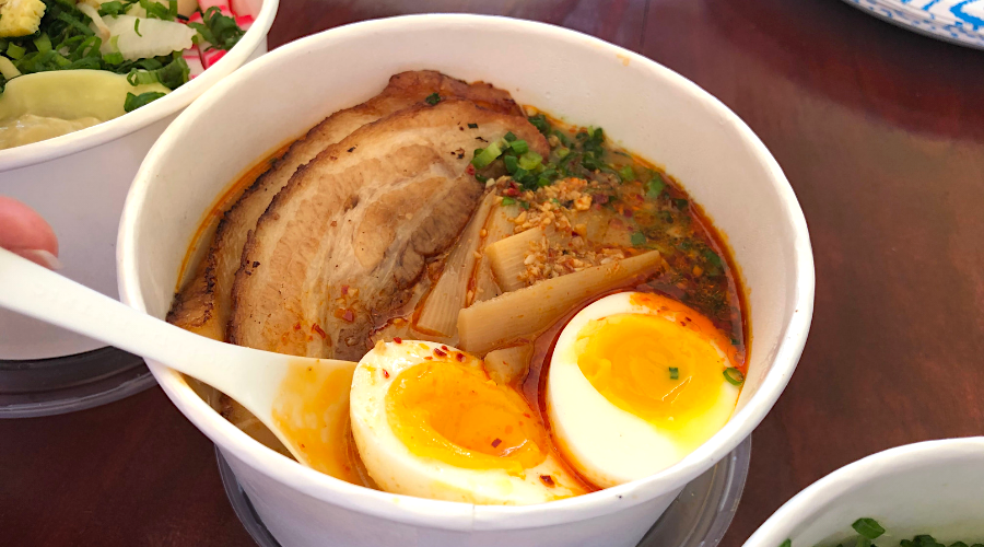 soft boiled eggs with oozy golden yolks and slices of roast pork top a takeout bowl of noodles