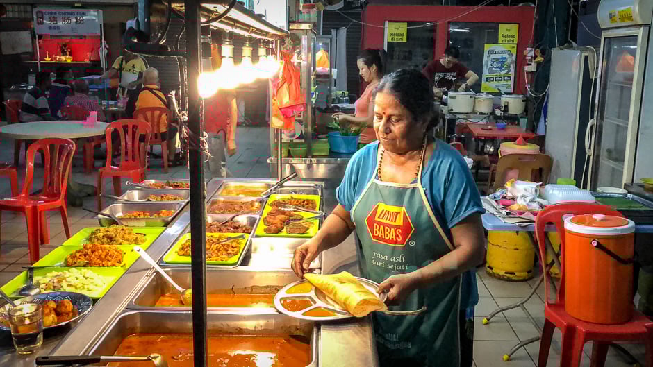 A woman prepares a thosa (dosa) plate with daal and curries (RM 4 or $1).