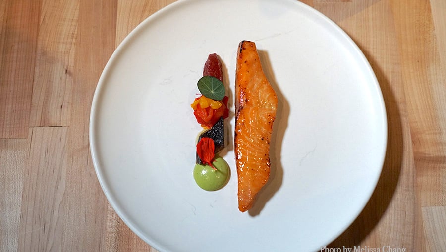 a sliver of grilled salmon rests next to a line of foams and garnishes