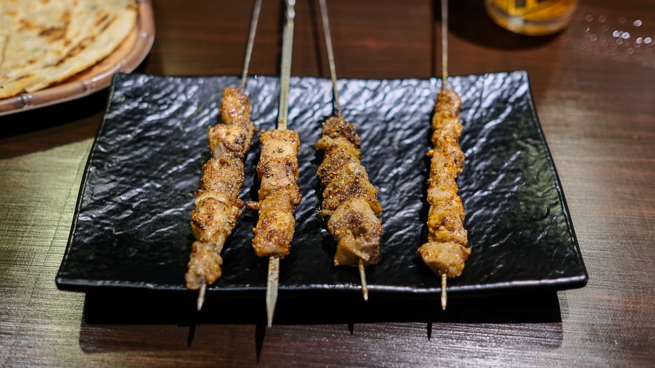 (L-R) Lamb, pork belly, beef brisket and tendon, and chicken tail skewers arranged on a plate.