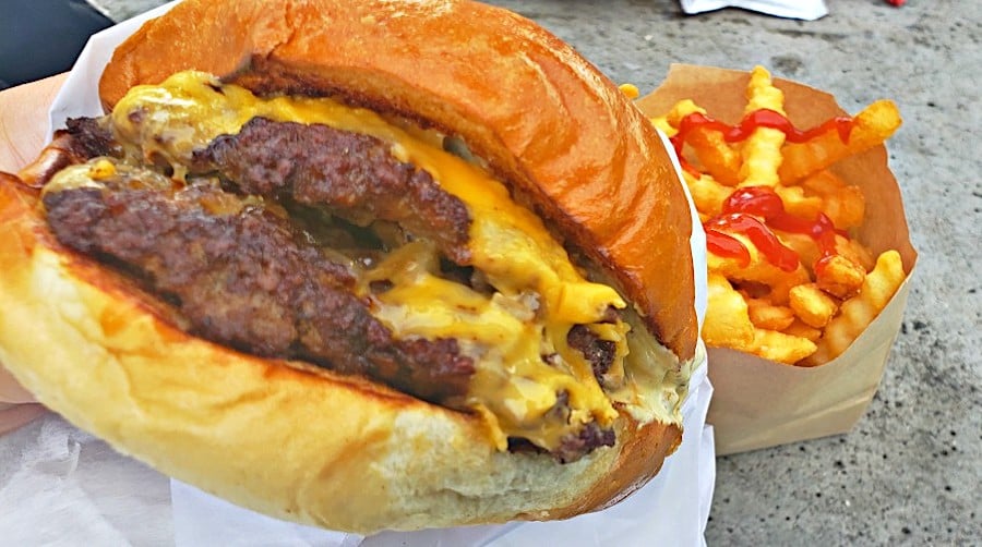 close-up of cheesy smash burger with fries and ketchup in background