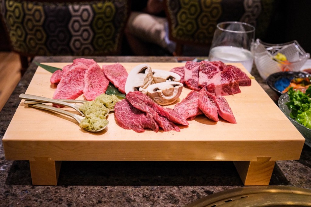 cuts of well-marbled a5 wagyu and king mushrooms await the grill on a pristine wooden geta at tableside