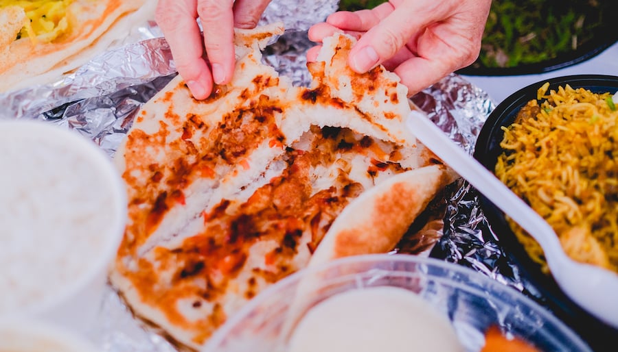hands tear a large round of indian dosa-style flatbread