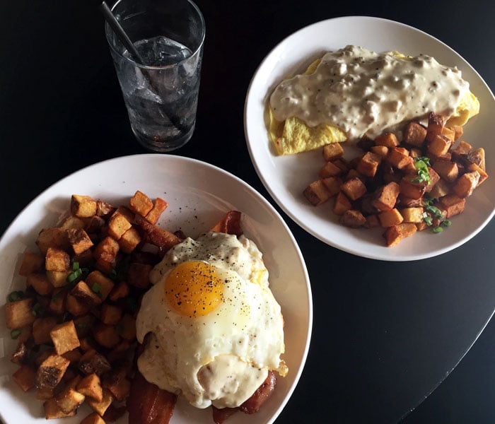 The Croque madame features hearty strips of bacon, béchamel, sunny side-up egg, and fried rosemary atop a buttermilk biscuit. The savory concoction comes with hand-cut fries or market greens.