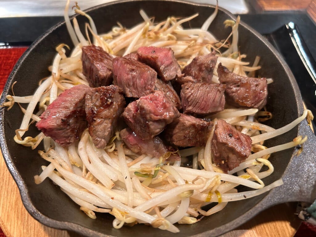 cubes of medium-rare steak on a bed of bean sprouts in cast iron pan