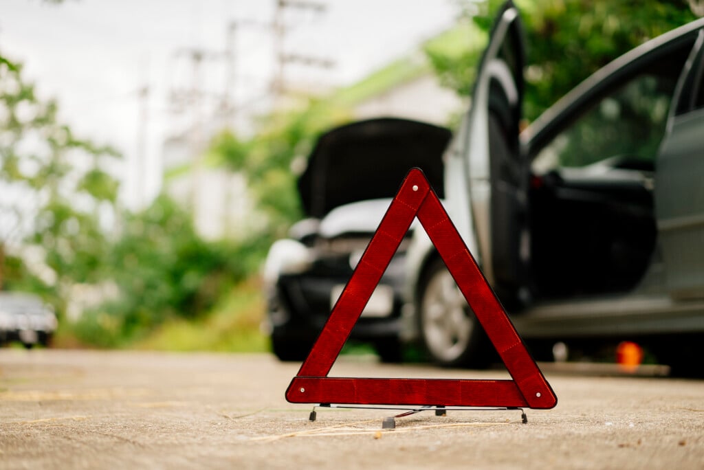 Insurance Adjuster Claim A Man In A Safety Vest Setting Up A Red Warning Triangle By A Car, Indicating A Breakdown Or Roadside Emergency.