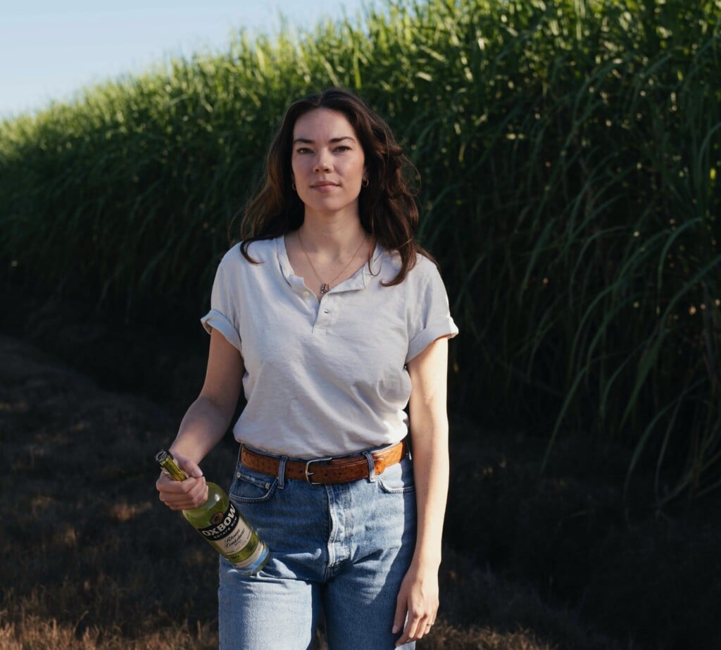 Oxbow Rum Distillery President Olivia Stewart at Alma sugarcane farm with Oxbow Rum bottle in hand