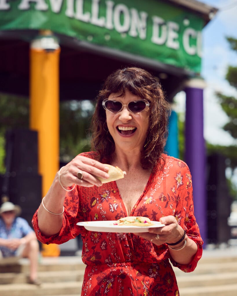 Woman at Festival International de Louisiane holding a taco in one hand and a plate with a taco in other hand.