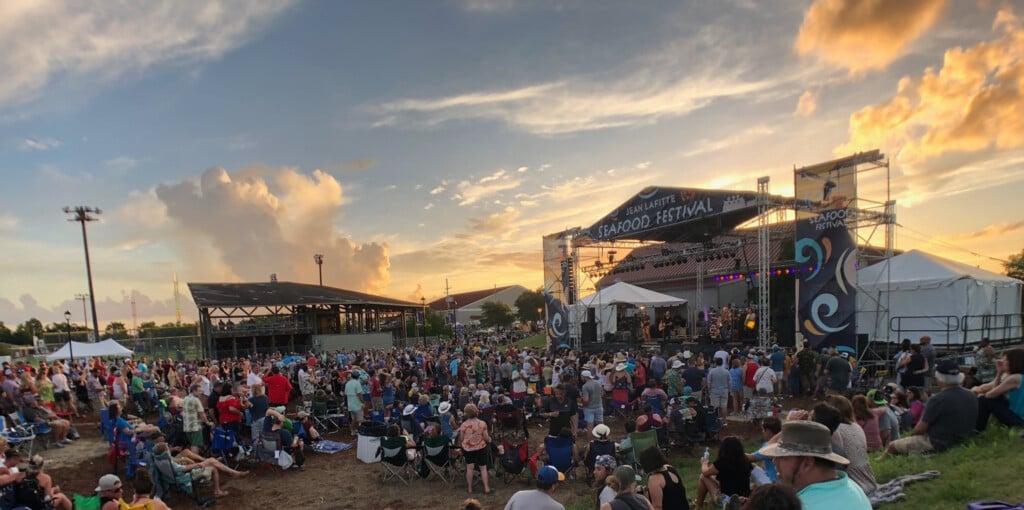 Crowd gathered standing and sitting on lawn chairs and the ground in front of a stage at the Jean Lafitte Seafood Festival