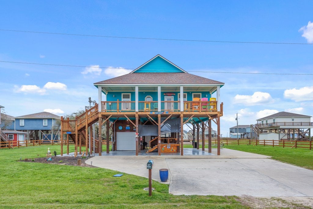 Padre's Oceanfront, Louisiana's Most-Wishlisted Airbnb in Cameron, La. Blue raised house with wooden stairs and balcony.
