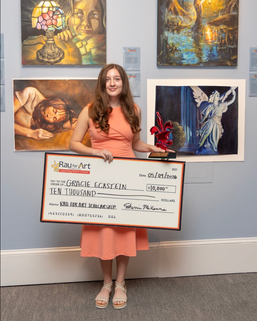 Rau for Art Scholarship First Place Winner Gracie Eckstein holding check standing in front of wall of artwork