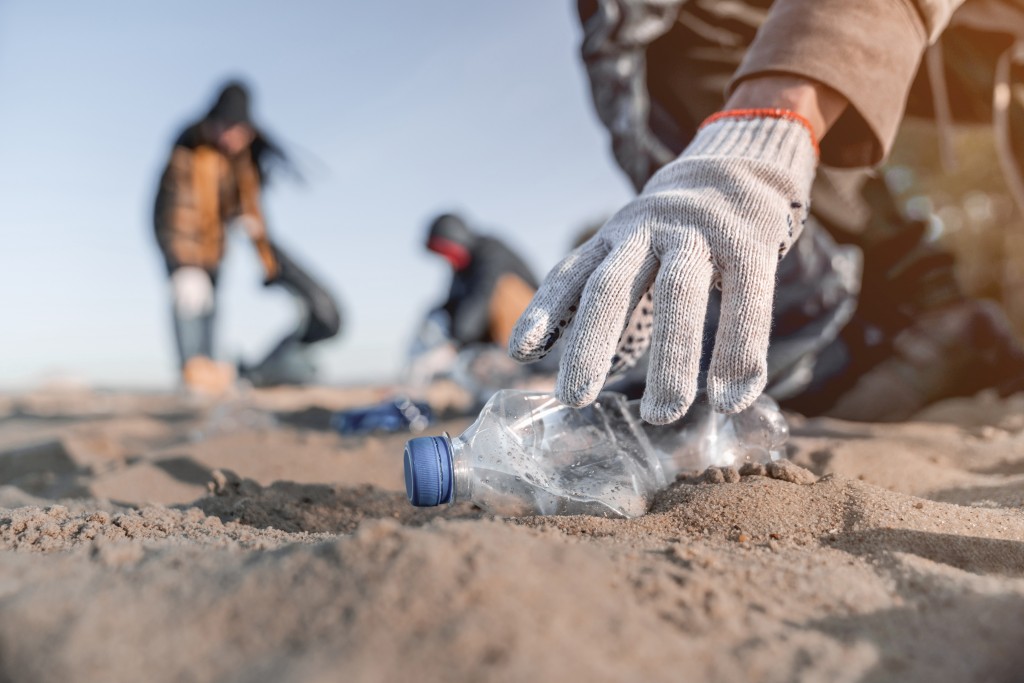 Volunteer Man Collecting Trash On The Beach. Ecology Concept