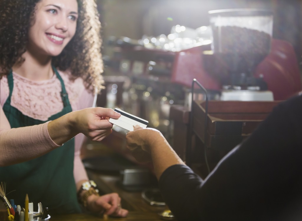 Cashier In Coffee Shop Takes Payment Card From Customer