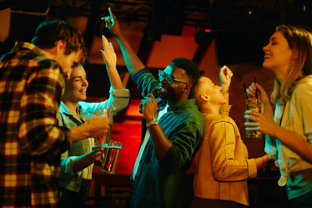 Happy Black Man Singing While Being On Karaoke Party With His Friends In A Pub.
