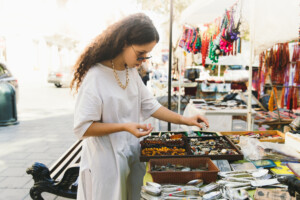 Young Woman With Curly Hair Shopping At Flea Market During Bright Sunny Day