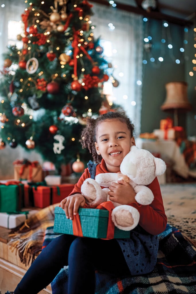 Portrait Of Smiling Black Little Girl With Teddy Bear And Gift Box On Christmas Looking At Camera.