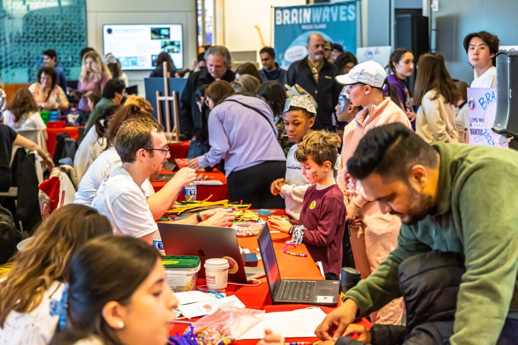 Adults and children participate in activities at tables during a busy indoor event.