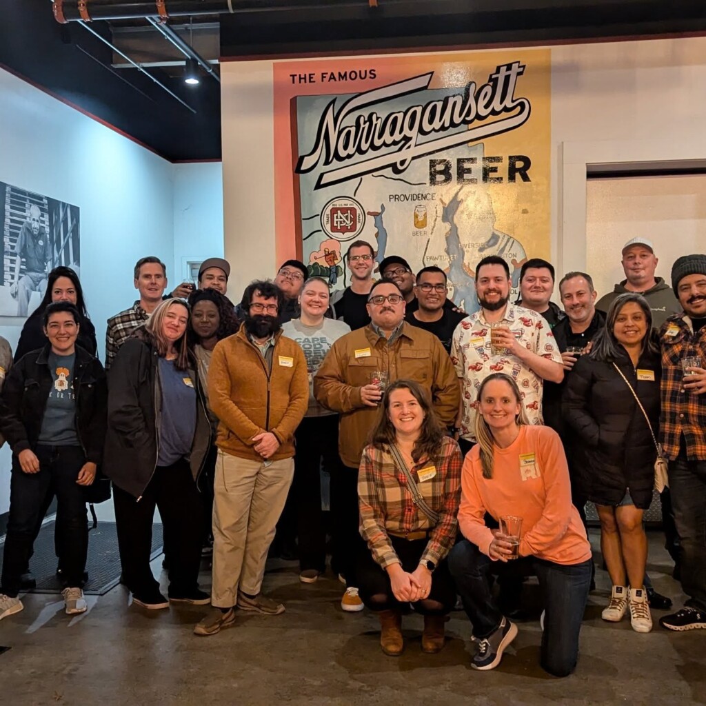 A group of casually dressed adults wearing name tags in front of a mural reading "Narragansett Beer."