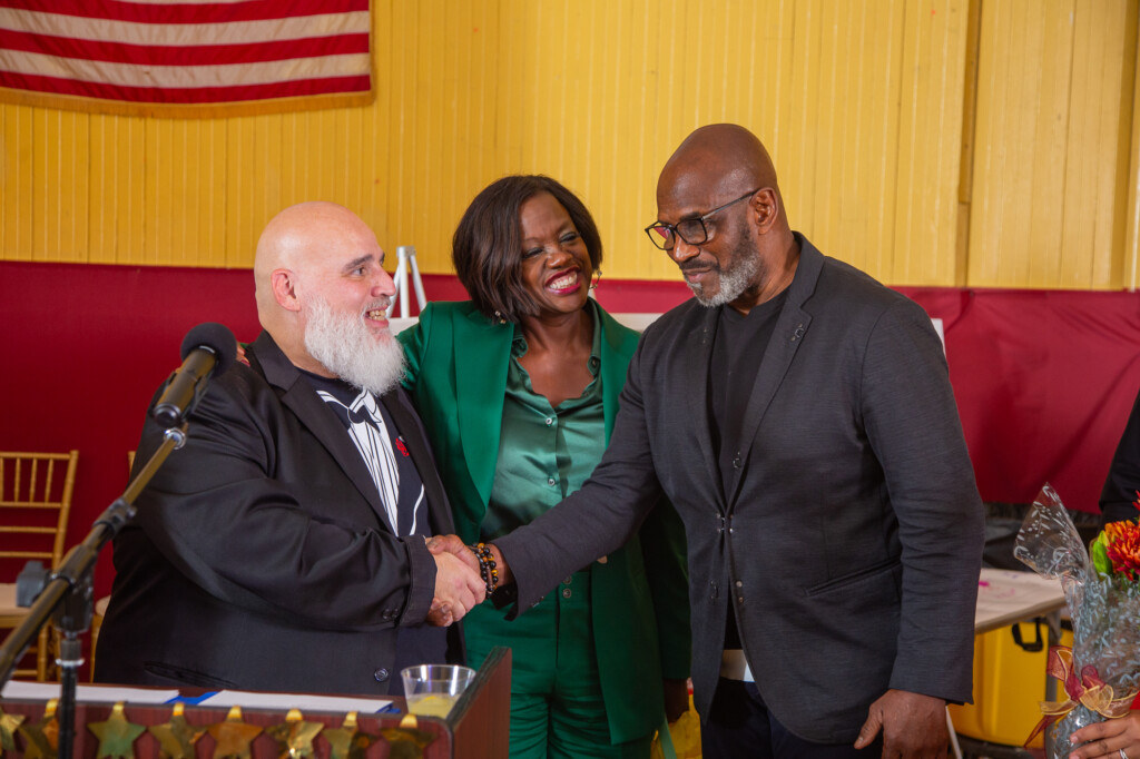 Angelo Garcia shakes hands with Julius Tennon while Viola Davis smiles during a formal event.