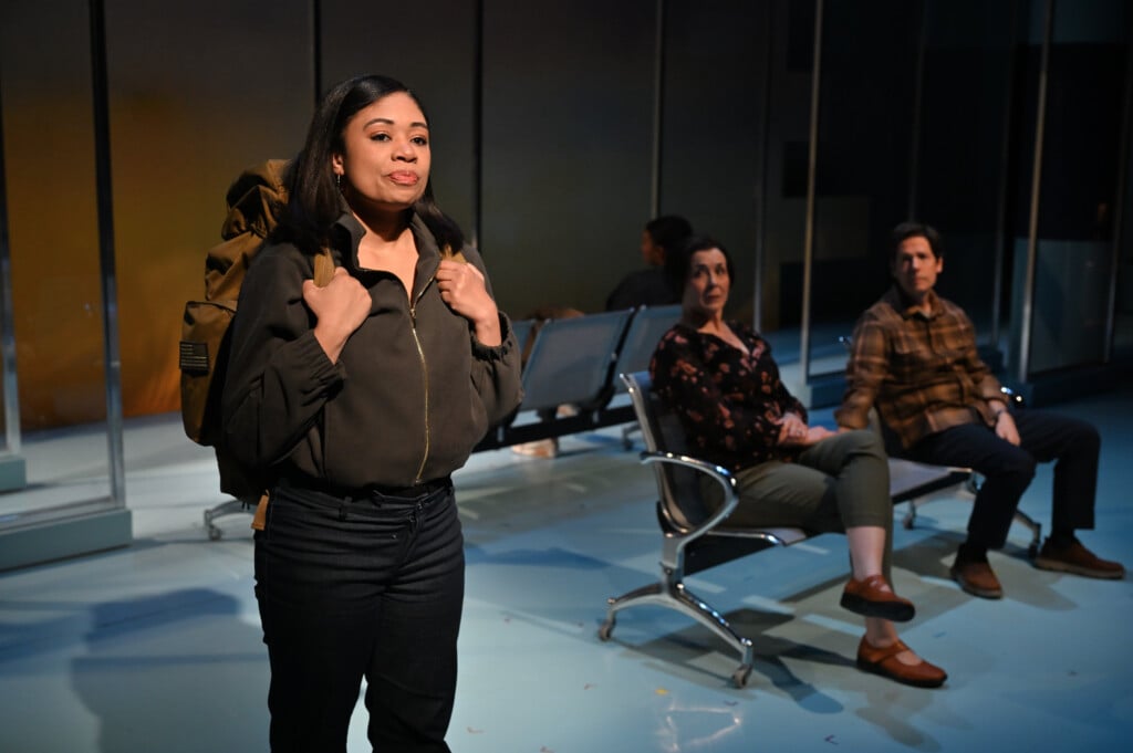 A young Latina woman stands in the foreground with a backpack while three other actors look on.