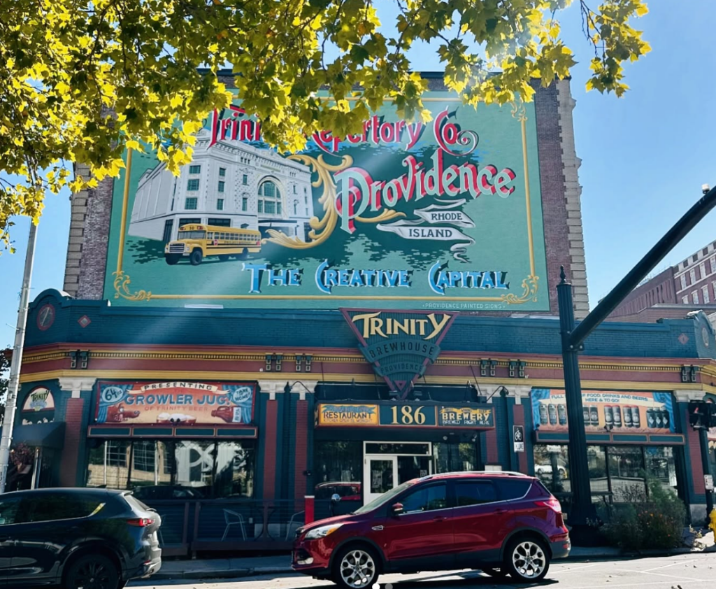 The front of a restaurant with a colorful mural featuring Trinity Repertory Company behind it.